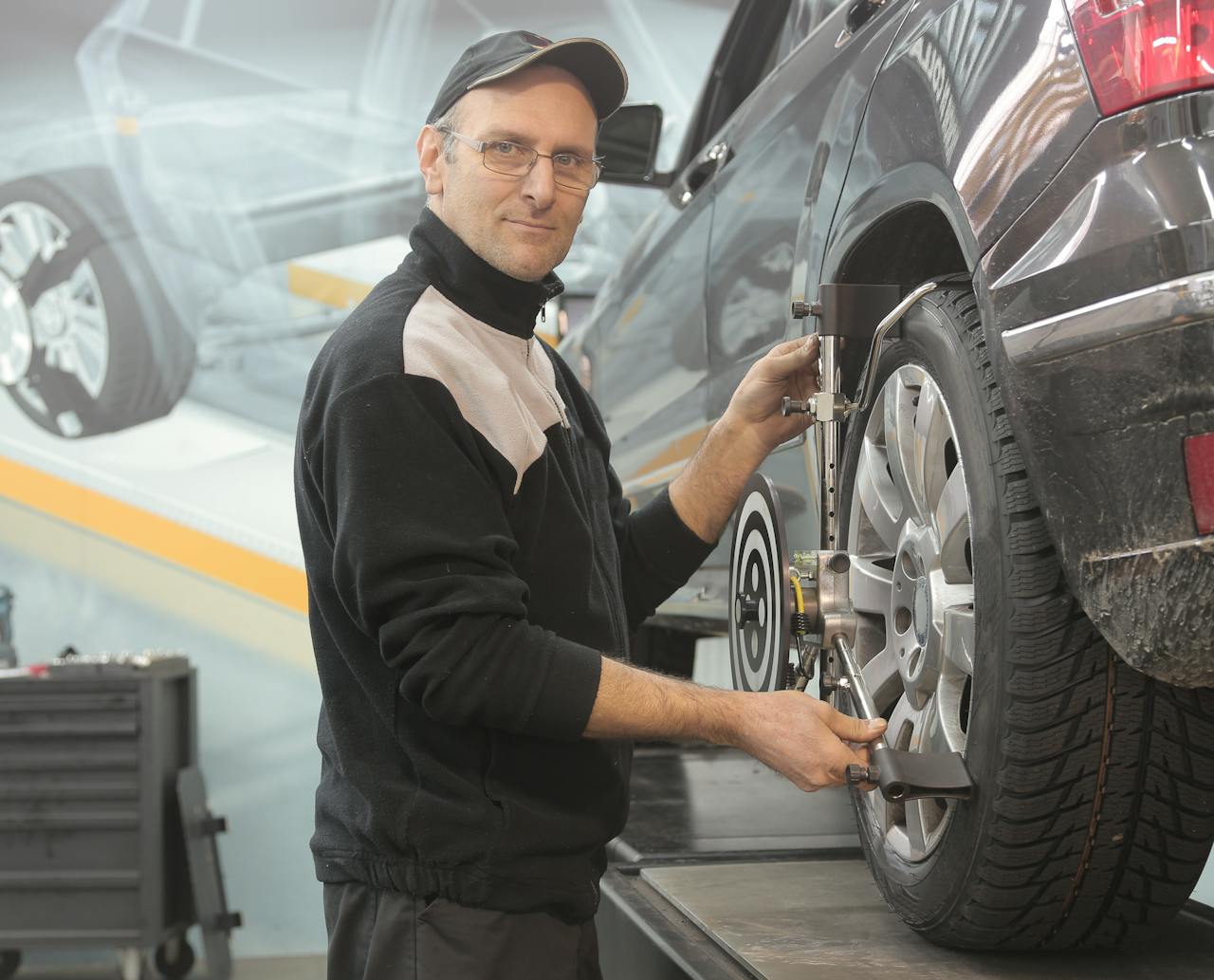 Home Mechanic performing wheel alignment on a car in a professional garage setting.